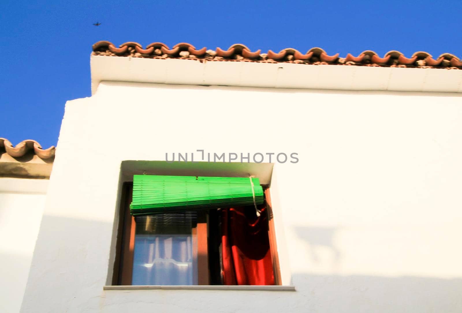 Whitewashed facade with window with green wooden blind in Altea village, Alicante, Spain