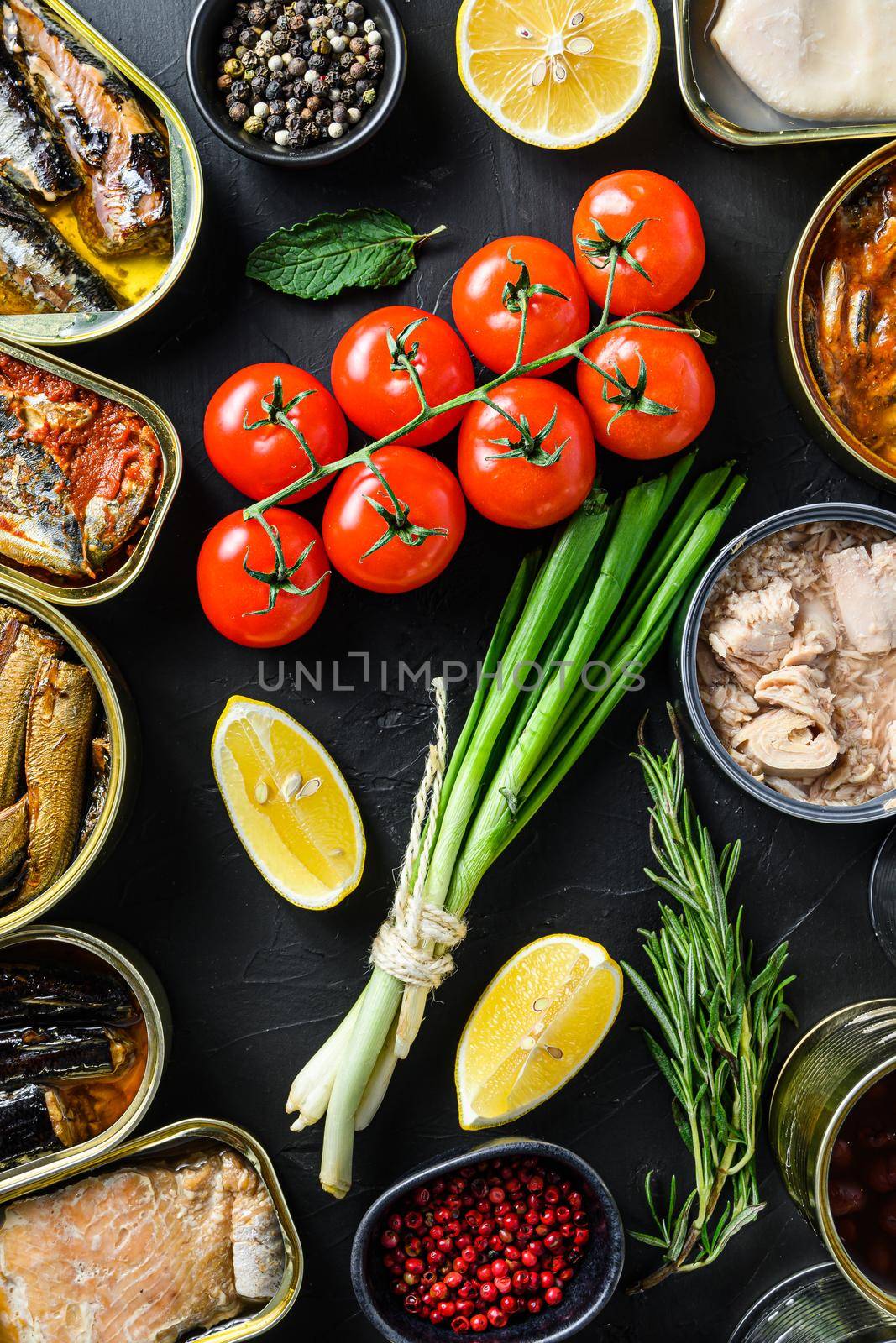 Mix of canned preserves food in cans with fresh organic bio ingredients tomatoe herbs lemon On the black chalkboard. Top view concept.