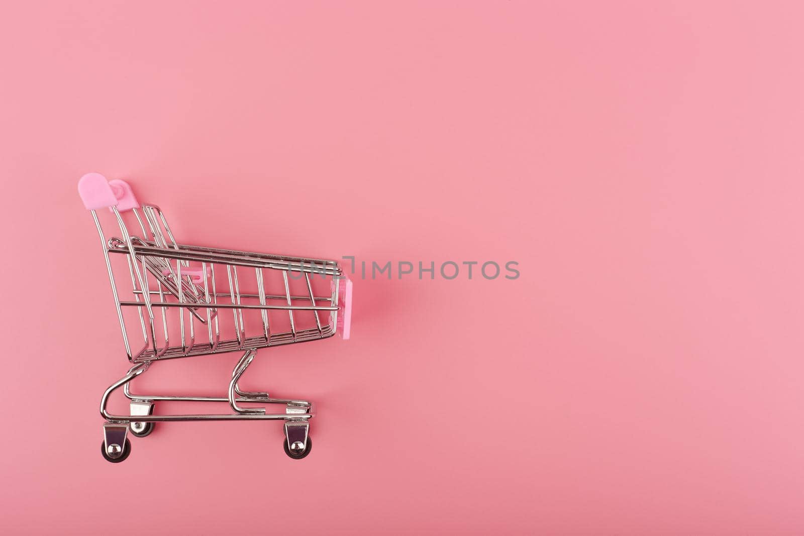 Creative flat lay with top view of toy shopping cart on pink background with copy space. Concept of online retail, sales and shopping. Template for commercial or advertisement