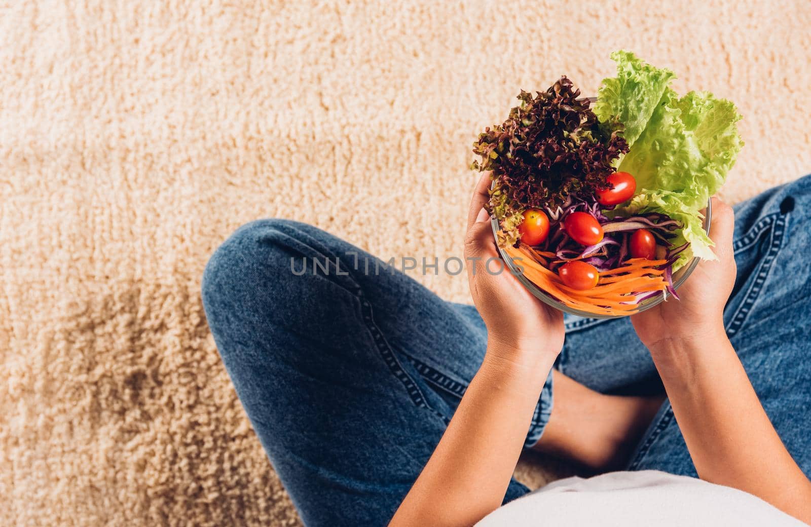 Young woman eating fresh salad meal vegetarian spinach in a bowl, top view of female hands holding bowl with green lettuce salad on legs, Clean detox healthy food concept