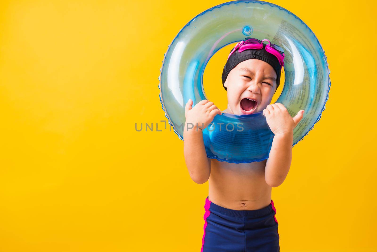 Summer vacation concept, Portrait Asian happy cute little child boy wear goggles and swimsuit hold blue inflatable ring, Kid having fun on summer vacation, studio shot isolated yellow background