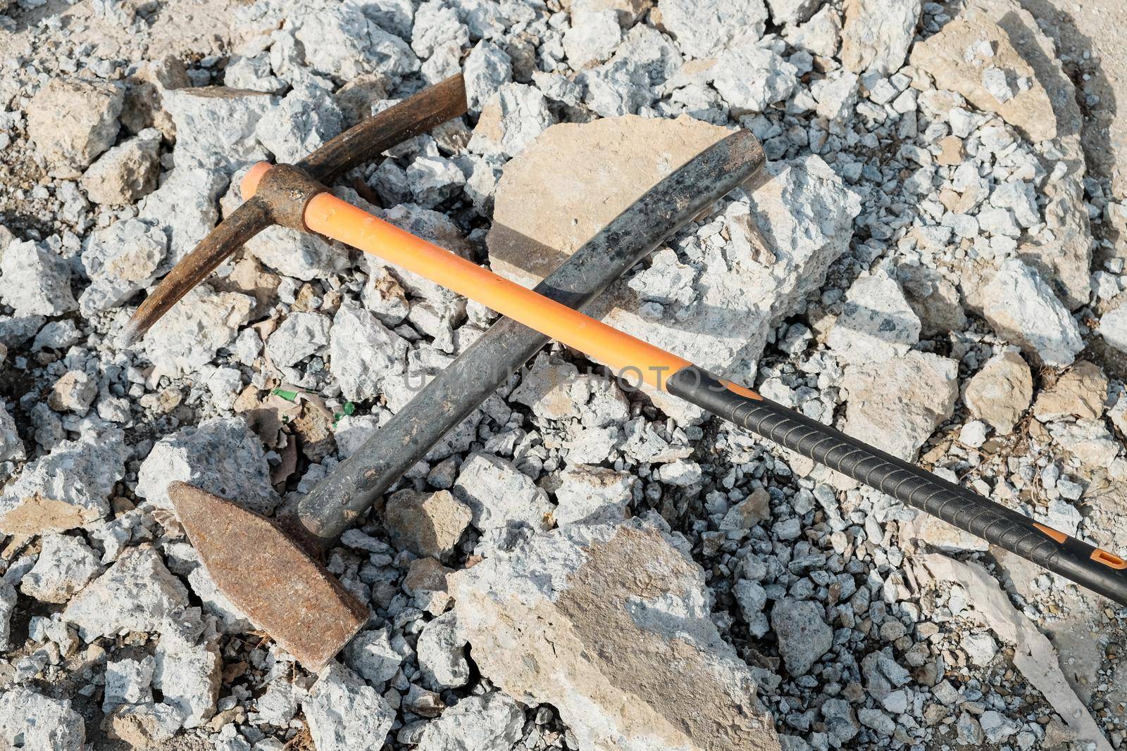 Geological pick with orange handle on the stones next to old hammer.