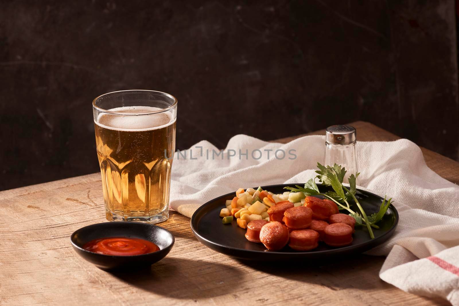 Glass of delicious beer with grilled sausages on wooden table