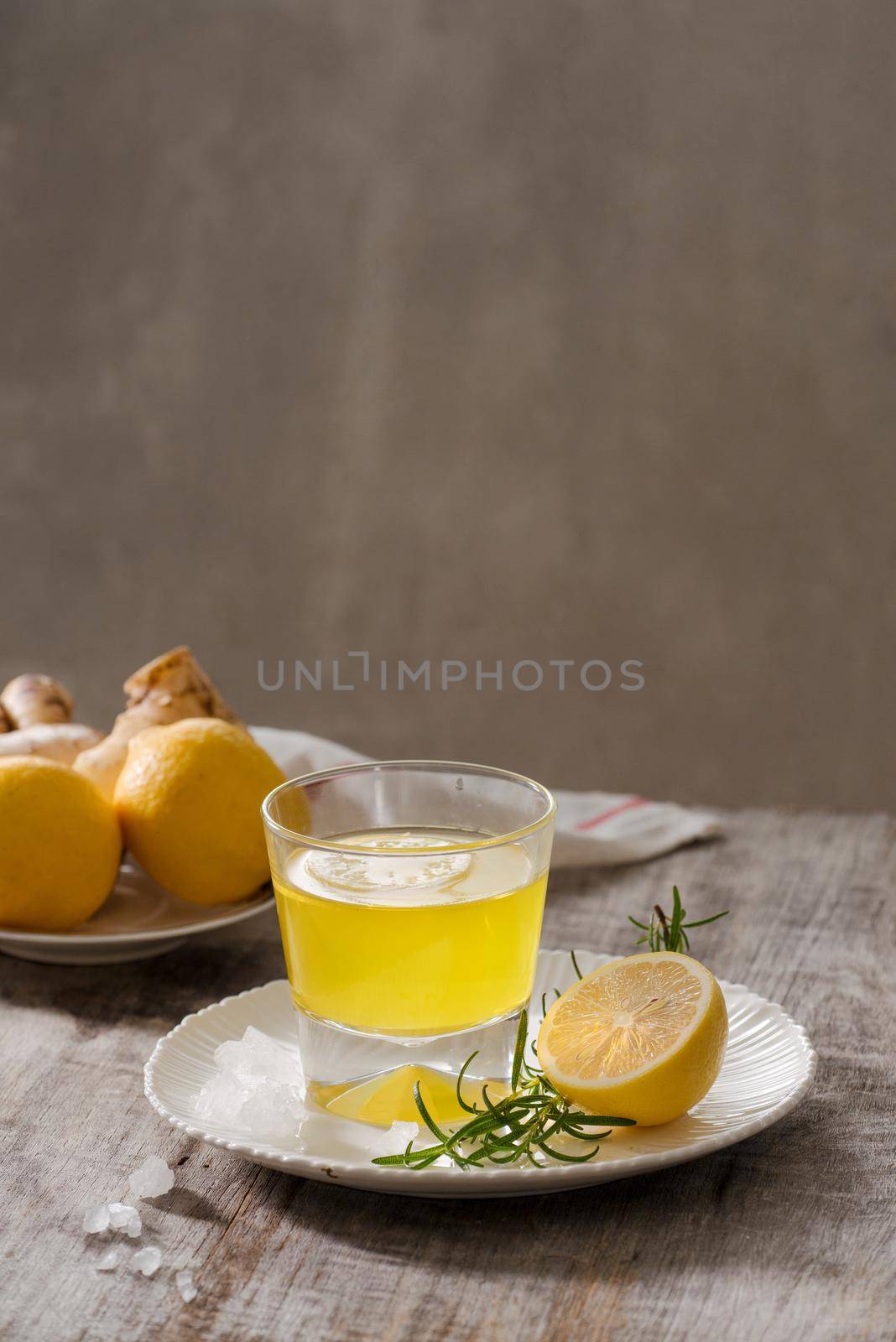 Ginger tea with lemon, ginger root and rosemarry on wooden background. Small glass transparent pitcher with hot drink. Seasonal beverages. Shallow DOF, selective focus, focus on top of pitcher.