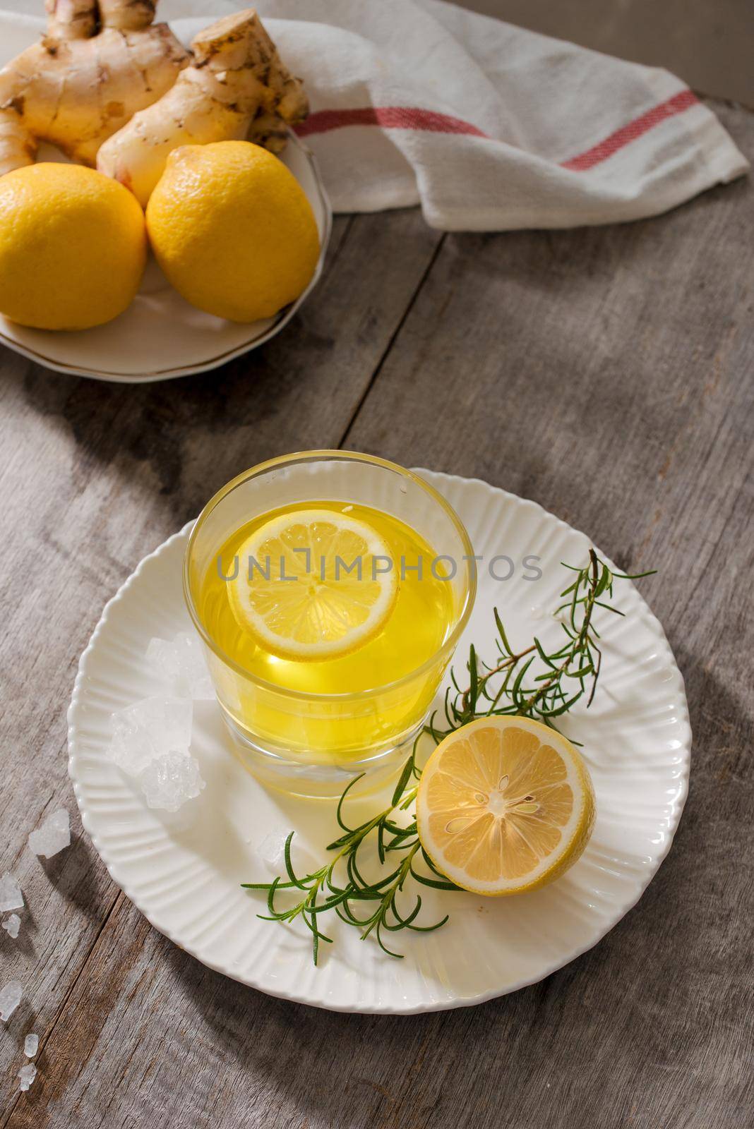 Ginger tea with lemon, ginger root and rosemarry on wooden background. Small glass transparent pitcher with hot drink. Seasonal beverages. Shallow DOF, selective focus, focus on top of pitcher.