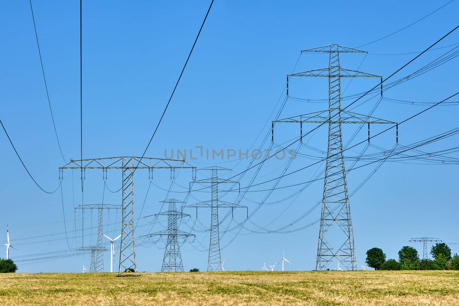 Electricity pylons and power lines with wind turbines in the background