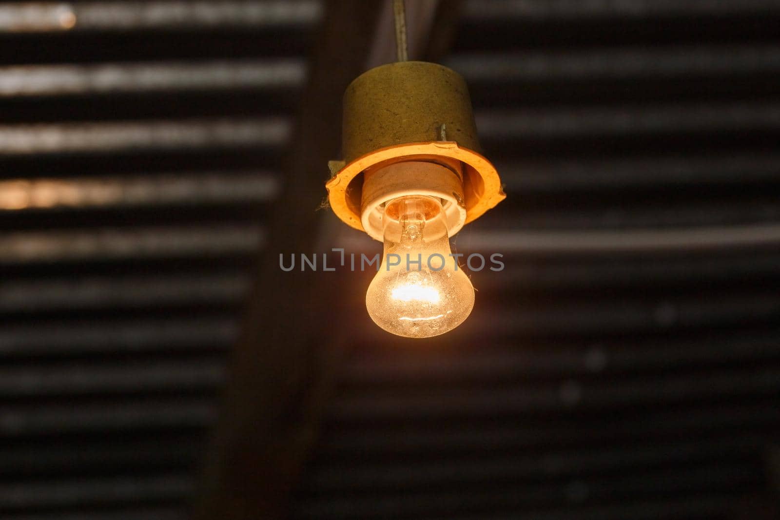 old dirty bare glass vacuum tungsten incandescent lamp lit under roof - close-up
