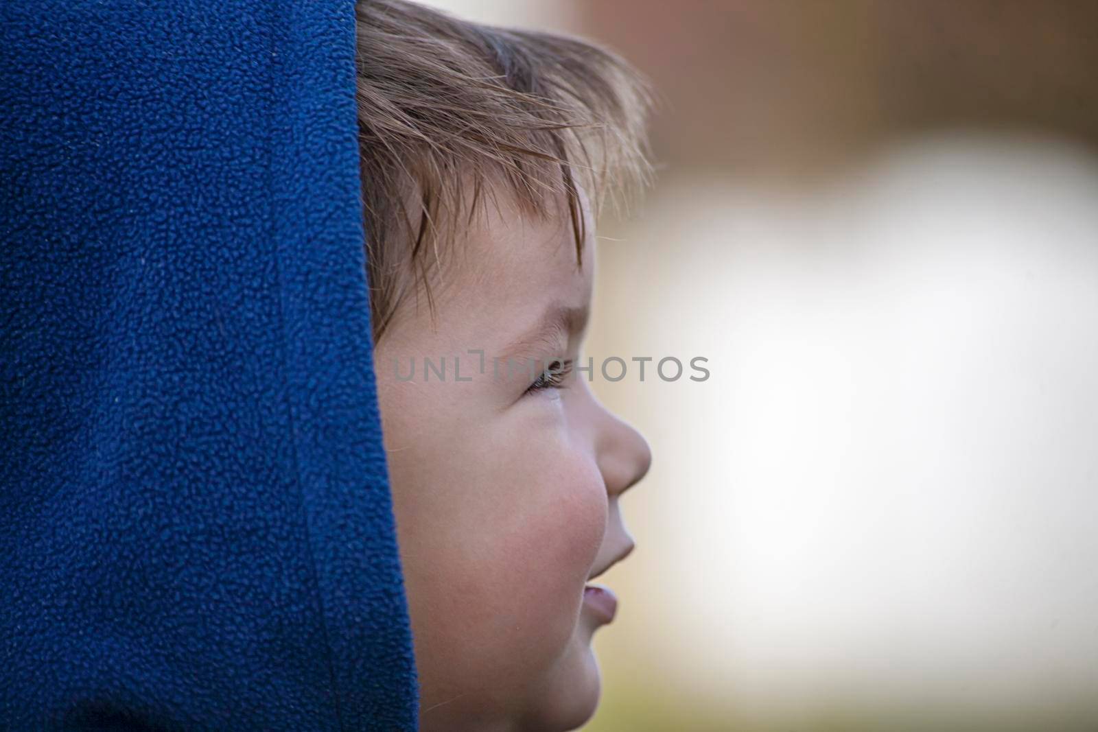 Child looking to one side and being  happy. Wearing blue hood.