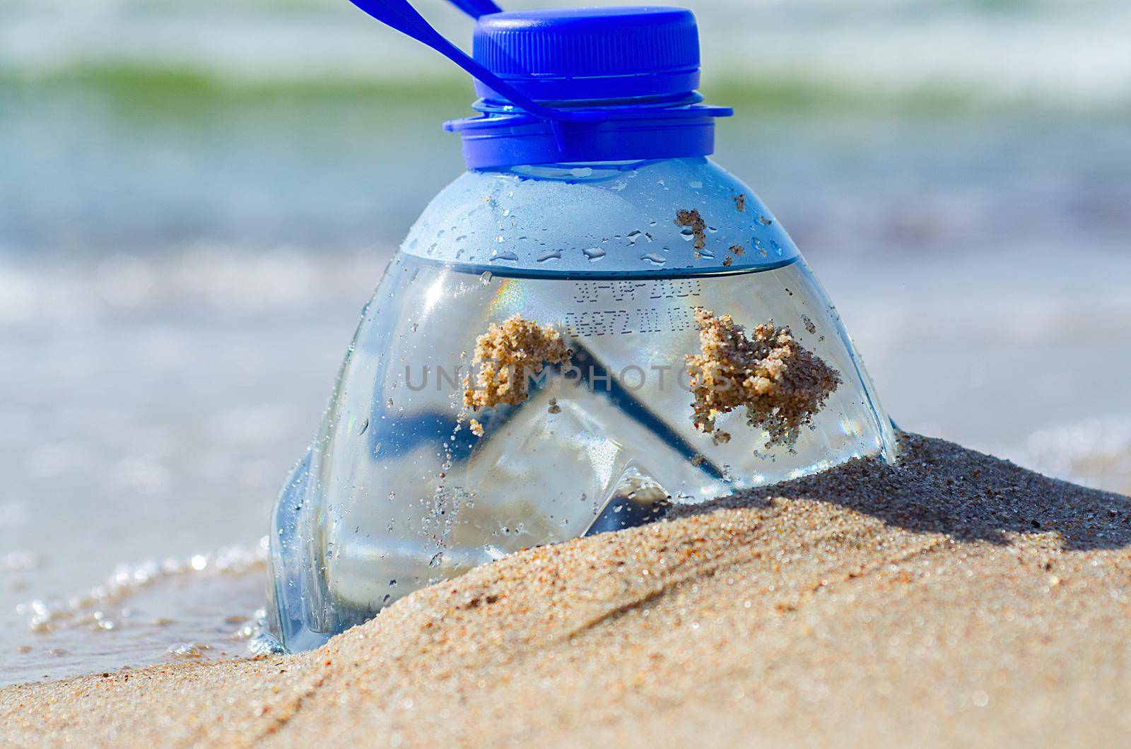 Package garbage on shore. Global warming problem. Bottle of fresh water by the sea.