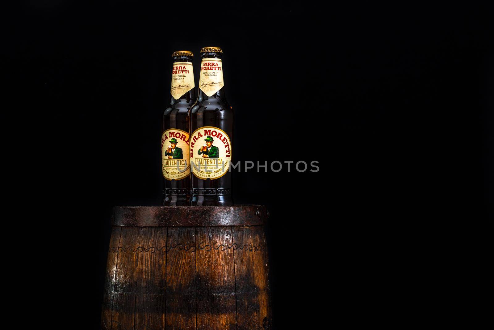 Bottle of Birra Moretti beer on wooden barrel with dark background. Illustrative editorial photo Bucharest, Romania, 2021 by vladispas