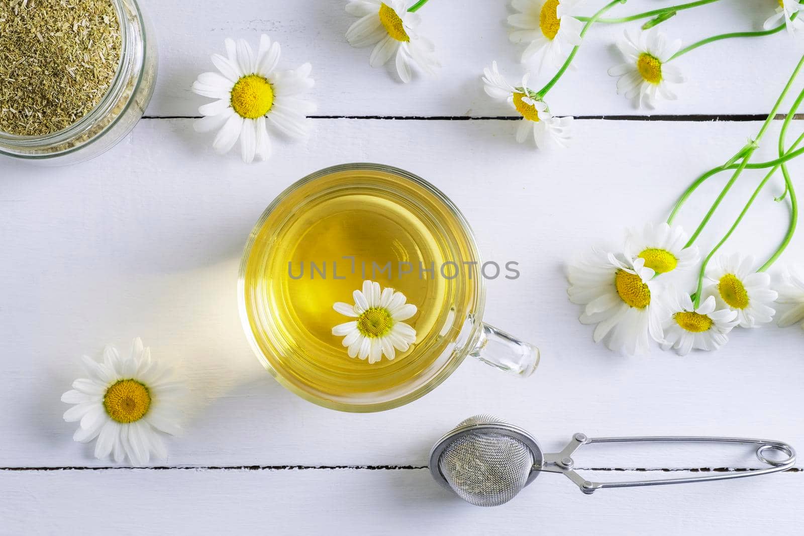 Close-up top view of a cup of chamomile tea, a can of dry raw materials and a spoon for infusion. Alternative and traditional medicine. Herbal treatment. Selective focus.