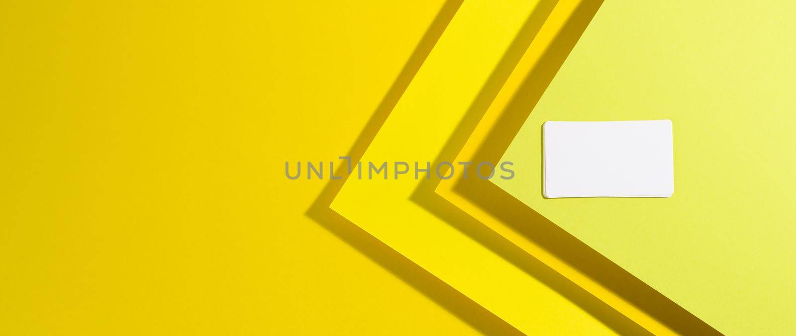 blank white rectangular business card on creative yellow background from sheets of paper with shadow, top view, copy space