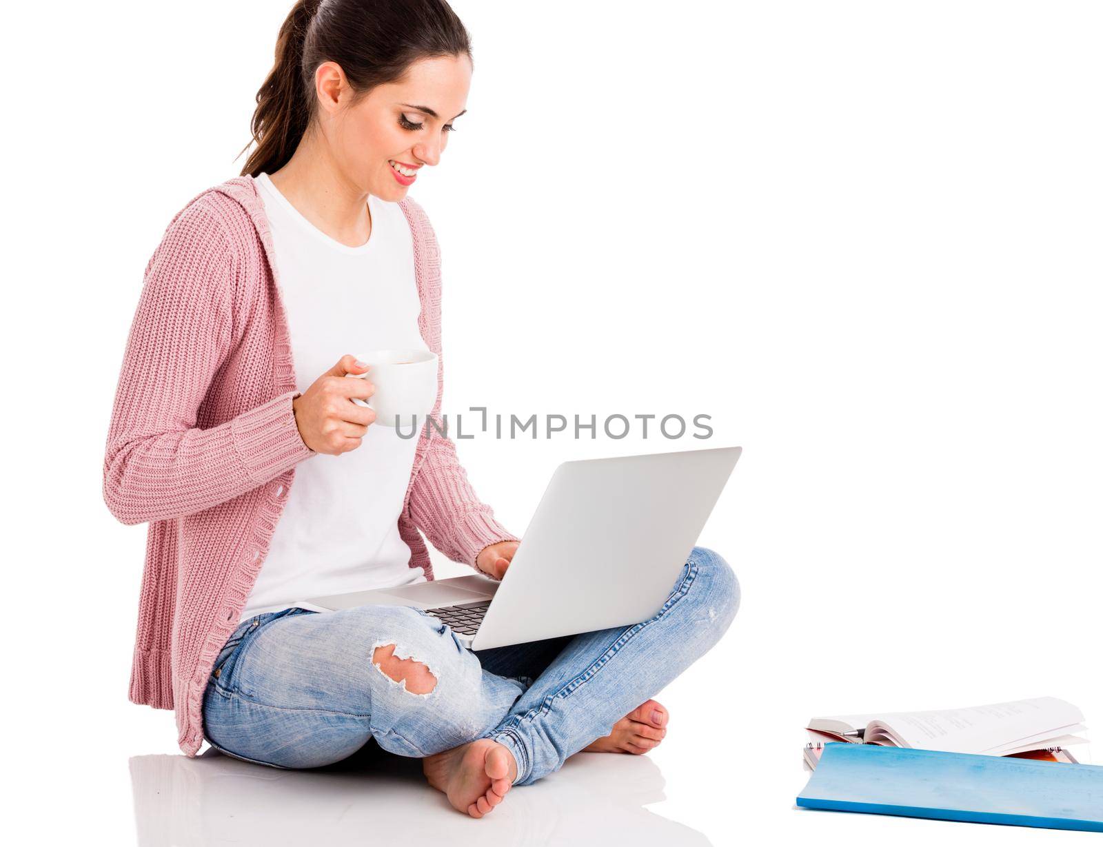 Beautiful woman sitting in the floor and working with a laptop while drinking coffee