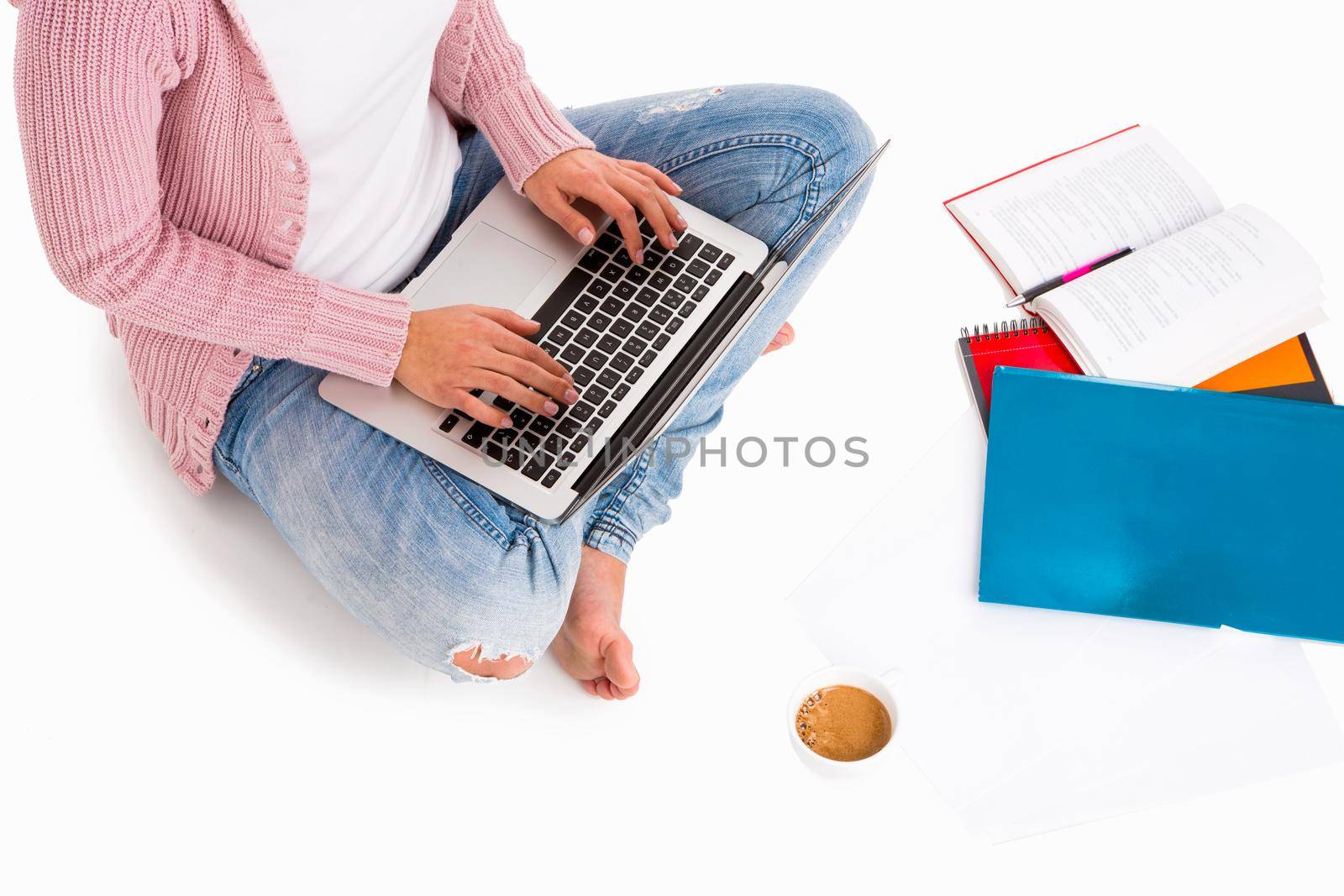 Young female student sitting with crossed legs working with a laptop, isolated over white background