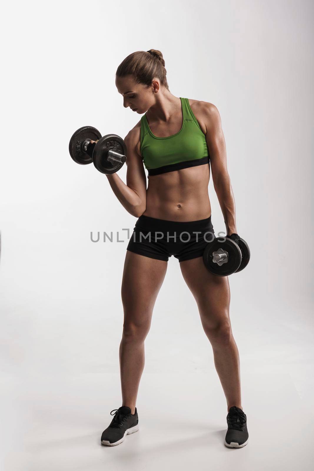 Beautiful young woman in a workout gear lifting dumbbells