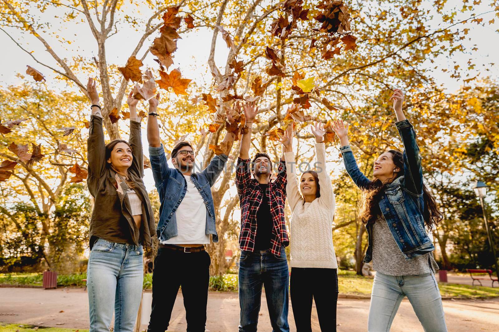 Group of friends in the park having fun throwing leaves in the air