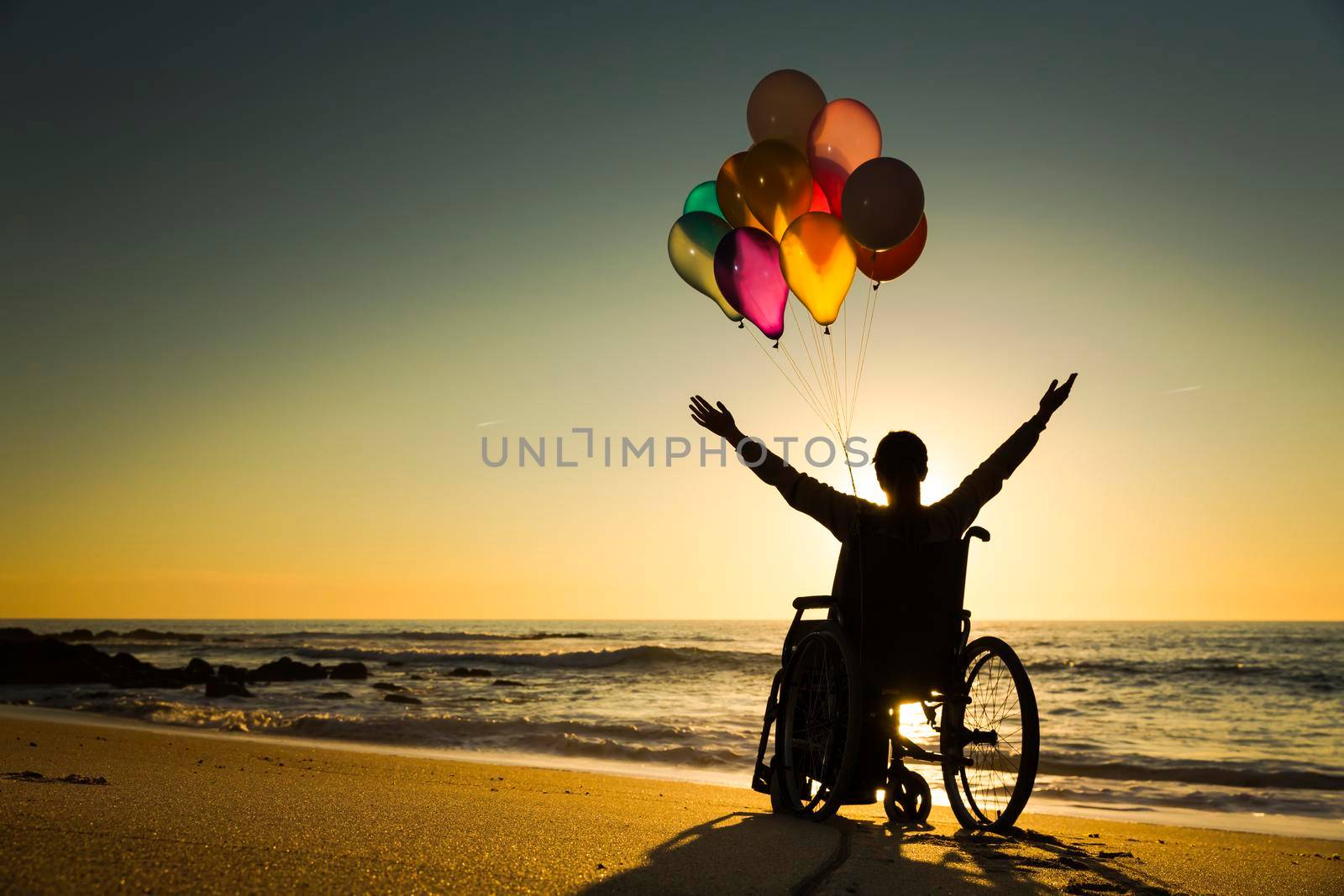 Handicapped man on a wheelchair with colored balloons at the beach