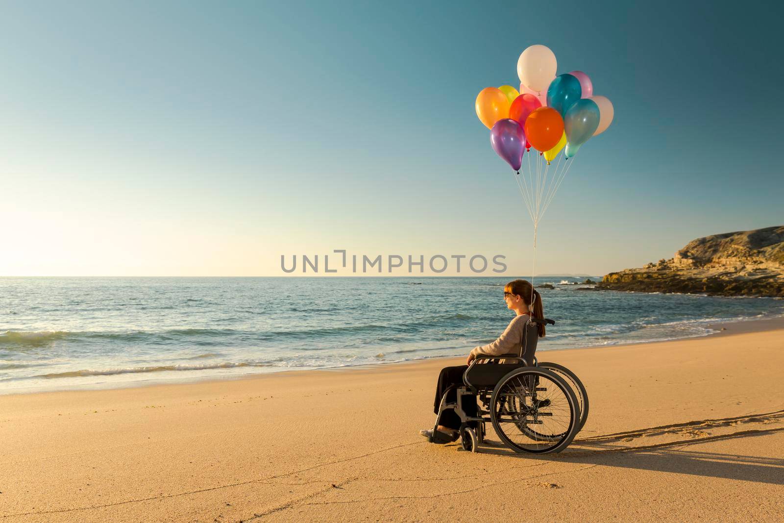 Handicapped woman on a wheelchair with colored balloons at the beach