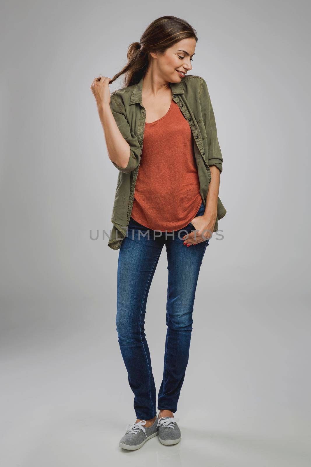 Beautiful young woman standing over a gray background touching her hair