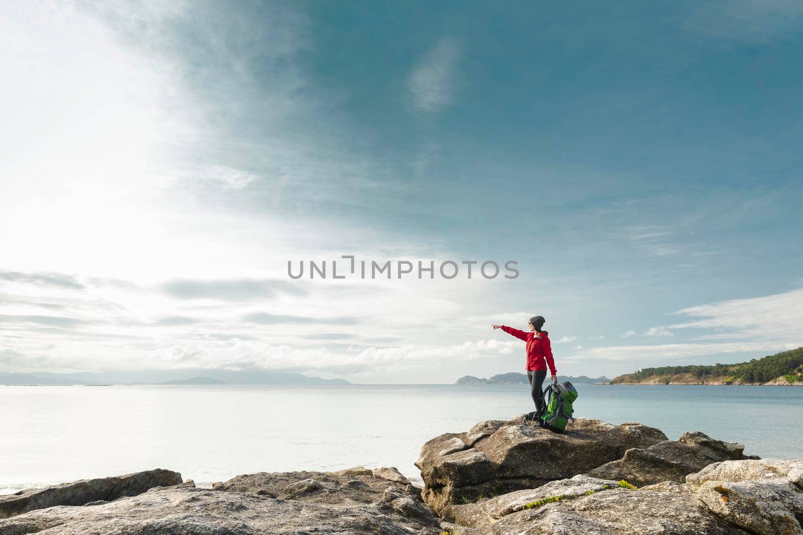 Woman with backpack enjoying and pointing to the beautiful morning view of the coast