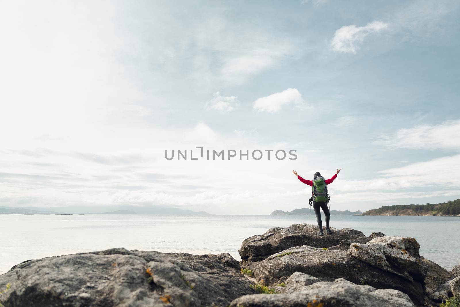 Woman with backpack and arms raised  enjoying the beautiful view of the coast