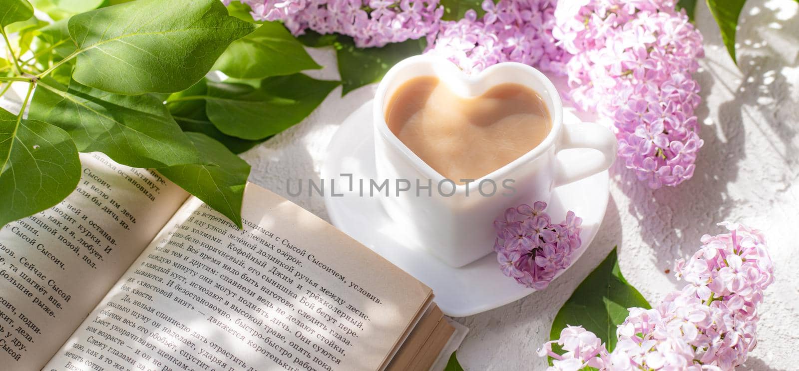 Cappuccino coffee in a cup with a book and a branch of lilac on a white background with shadows . A hot drink. Reading books. relax. Cafeteria advertising concept. Article about cappuccino. Making cappuccino. Lilac branches. Spring. Copy space