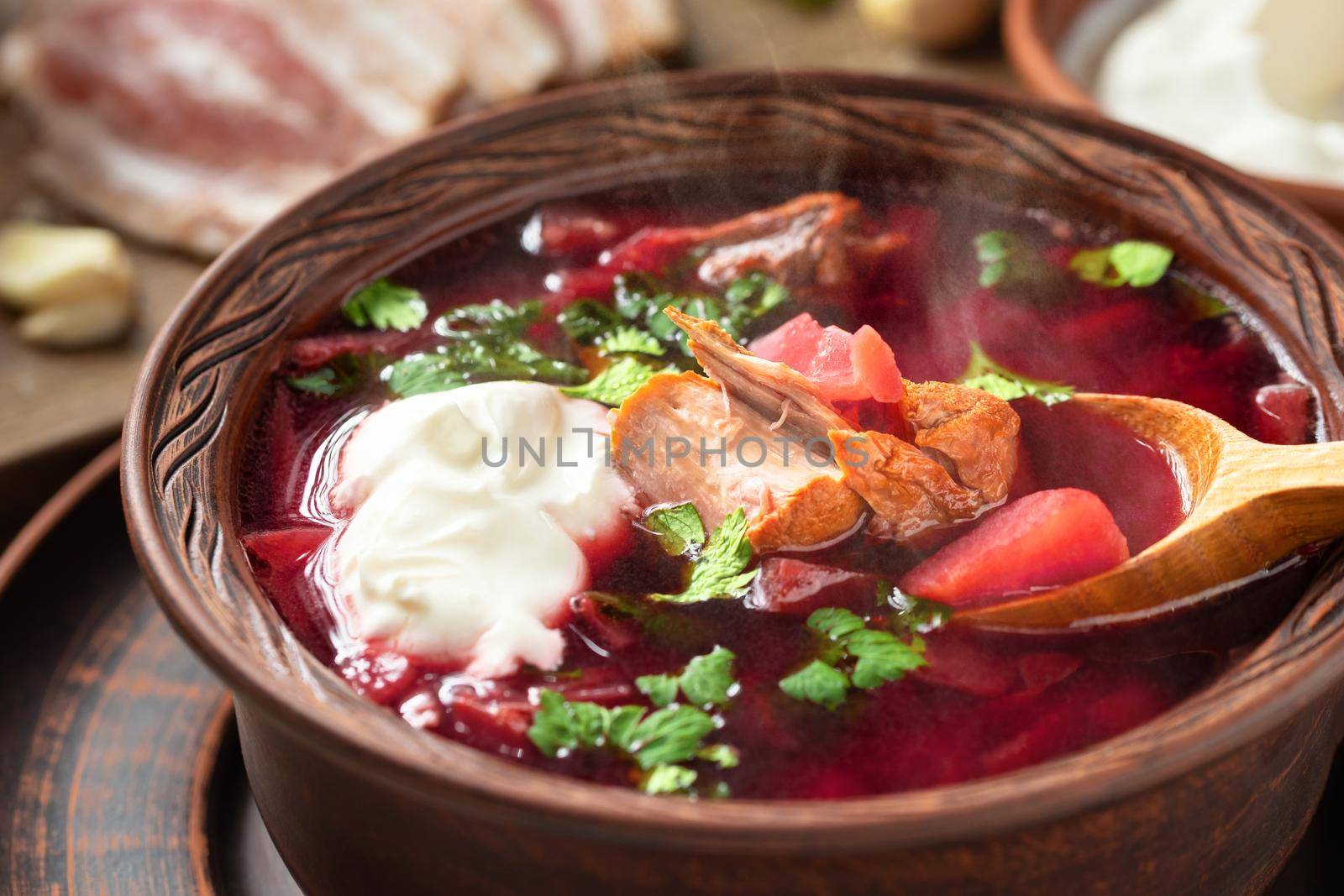 Freshly cooked borscht - traditional dish of Russian and Ukrainian cuisine in earthenware dishes with bacon, bread, sour cream and garlic, close up.