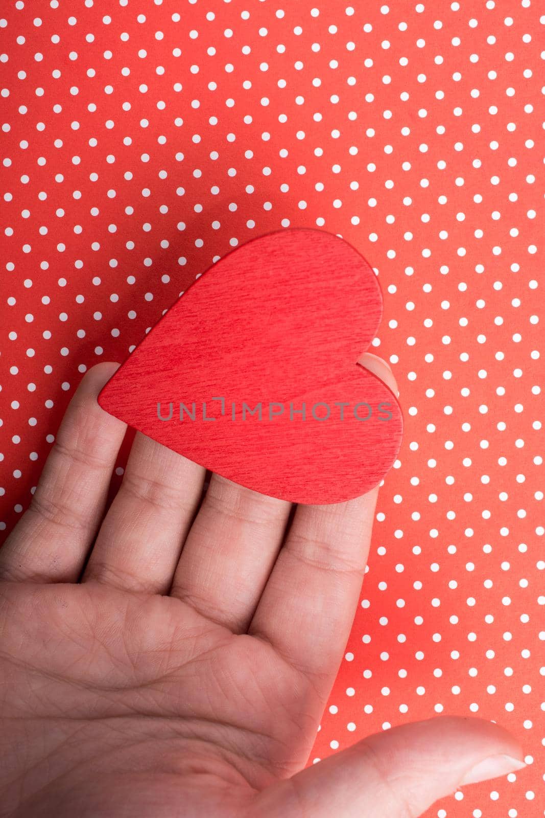 Red color heart shaped object in hand  on dotted paper