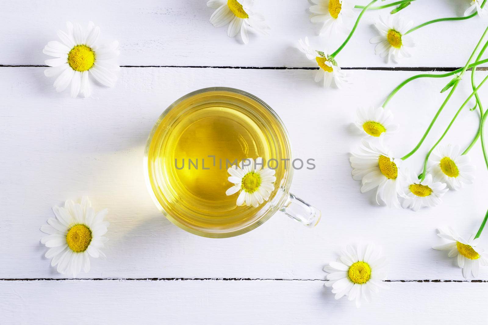 Close-up top view of a glass cup of chamomile tea and chamomile flowers. Folk and alternative medicine. Herbal treatment. Selective focus.