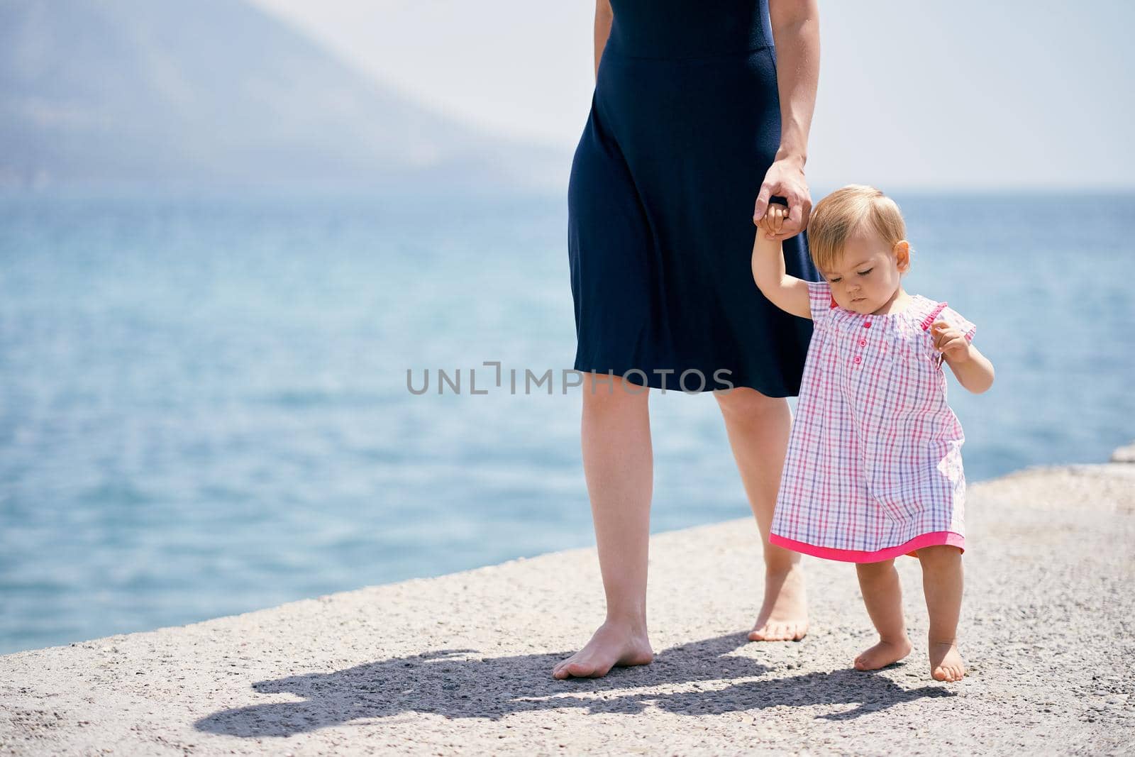 Mom leads a little girl by the hand along a concrete breakwater by Nadtochiy
