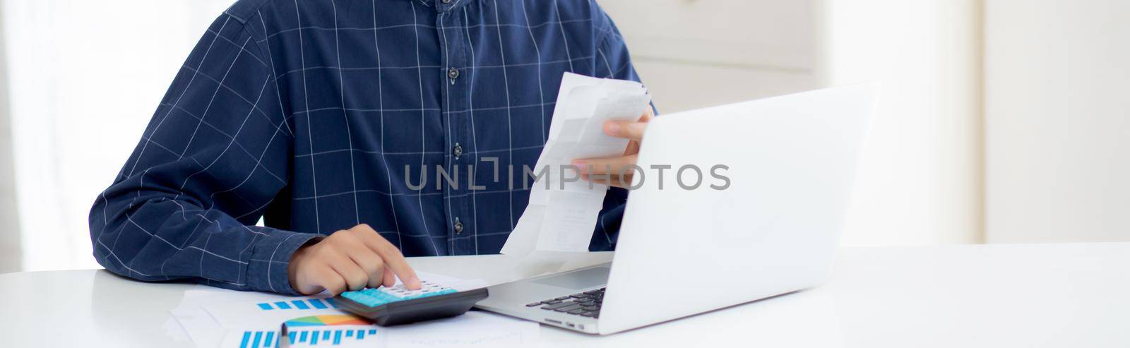 Young asian man calculating finance household with calculator on desk at home, male checking bill and success for saving expenses household, debt closure, tax and accounting, business concept.