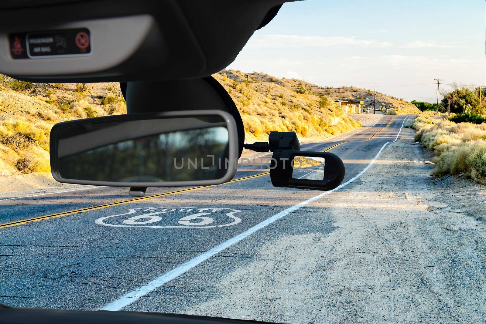 Looking through a dashcam car camera installed on a windshield with view of the Historic Route 66, with pavement sign in California, USA