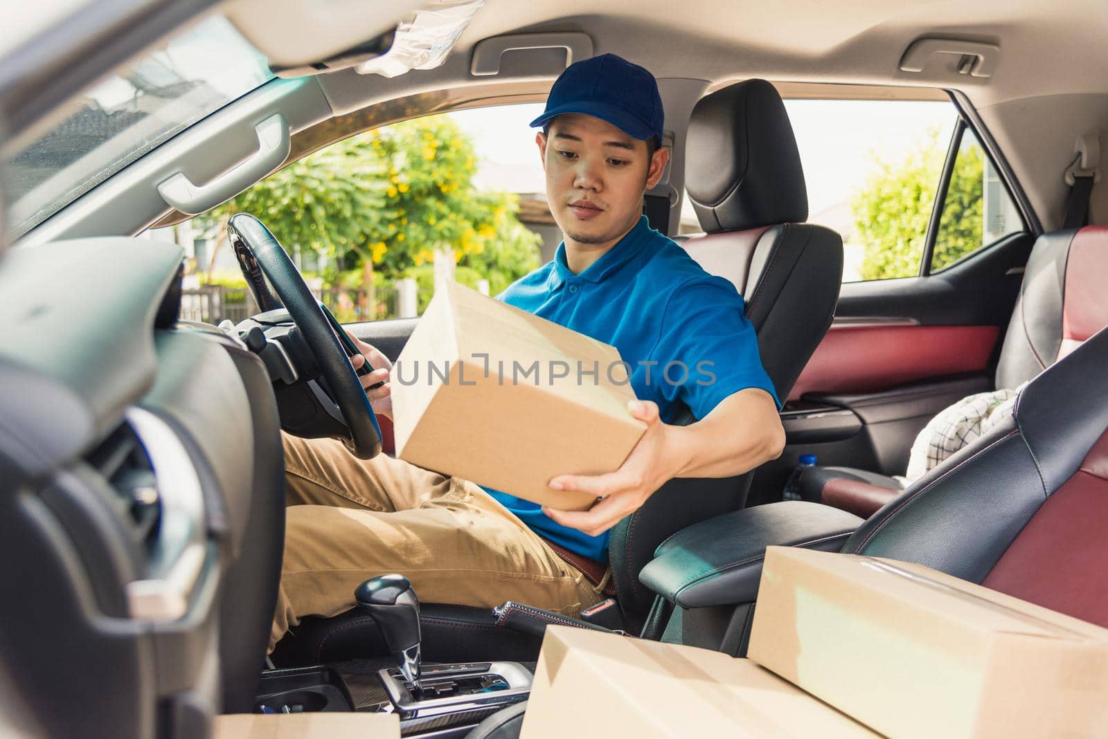 delivery man courier in uniform hold documents clipboard checking list parcel post boxes inside a car by Sorapop
