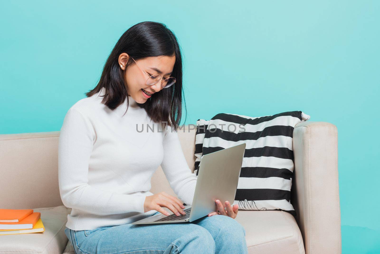 woman wear eyeglasses sitting on sofa using a laptop by Sorapop