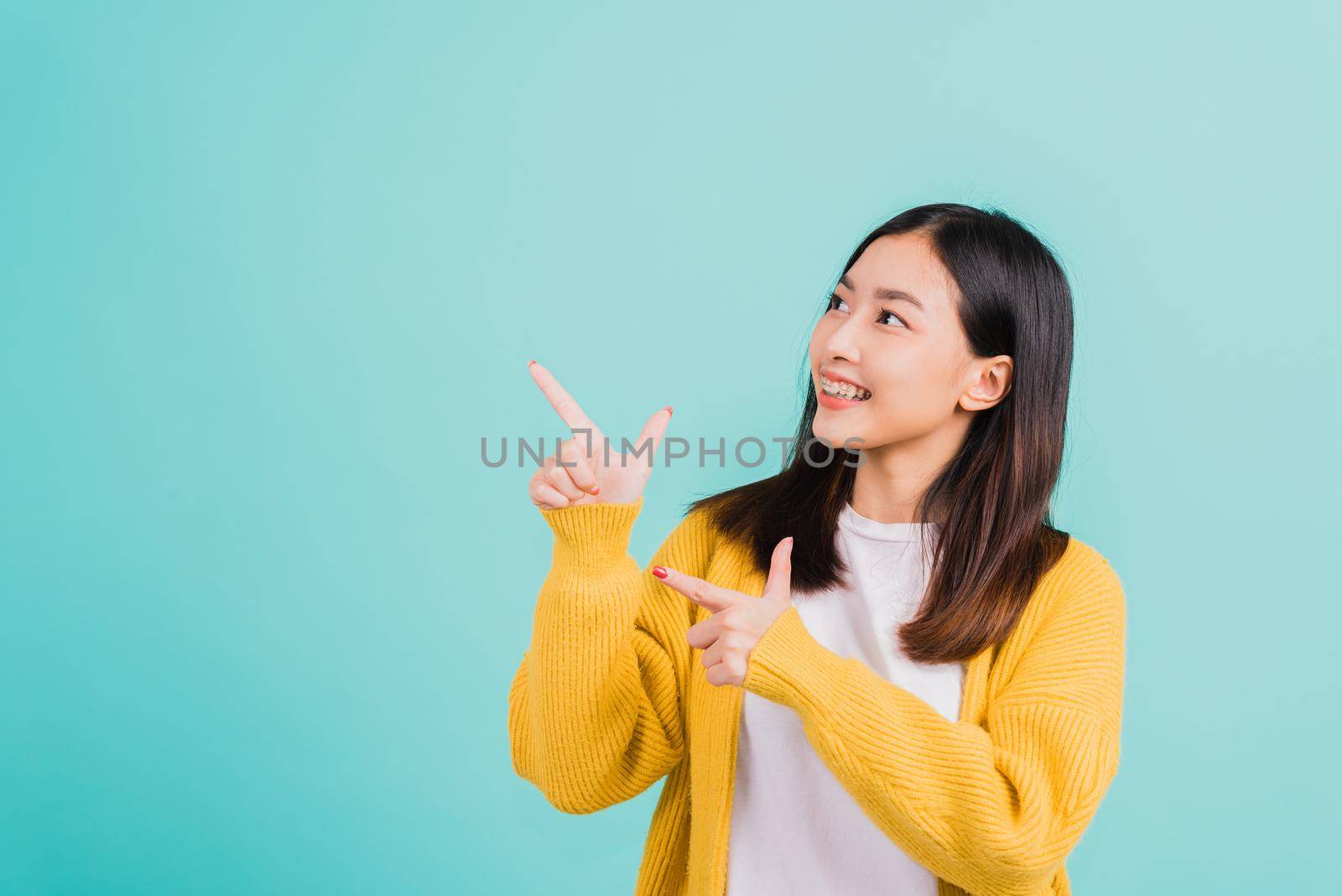 Portrait Asian beautiful young happy woman teen smiling show white teeth she's pointing finger up to side empty space studio shot isolated on blue background, Dental health concept