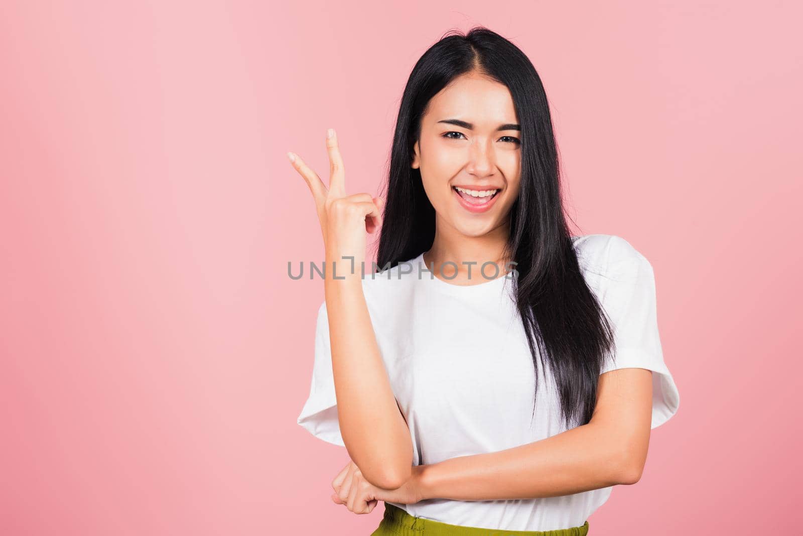Asian happy portrait beautiful cute young woman teen smile standing show finger making v-sign victory sign gesture side away looking to camera studio shot isolated on pink background with copy space