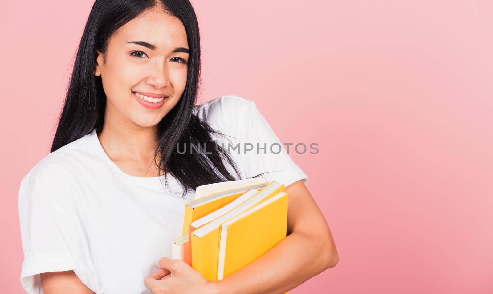 Portrait of beautiful Asian young woman teenage smiling hugging books, female person holding book multicolor, studio shot isolated on pink background with copy space, education concept