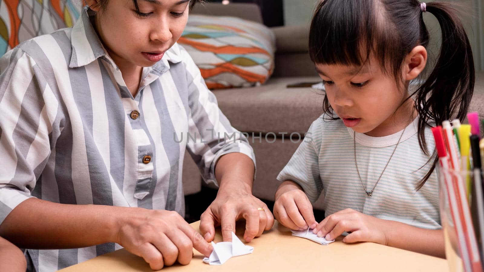 Mother and children learning about The Japanese art of folding paper into decorative shapes and figures at home. by TEERASAK