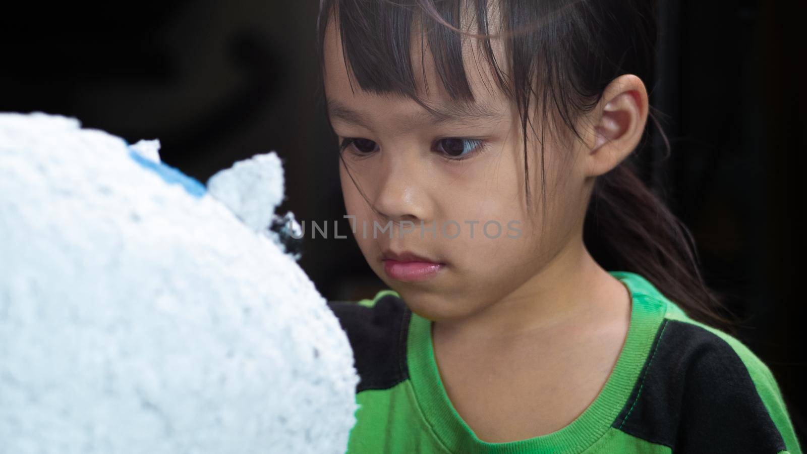 A little girl paints with a brush on the figure of a white pig-shaped papier-mache at home. Make your own piggy bank.