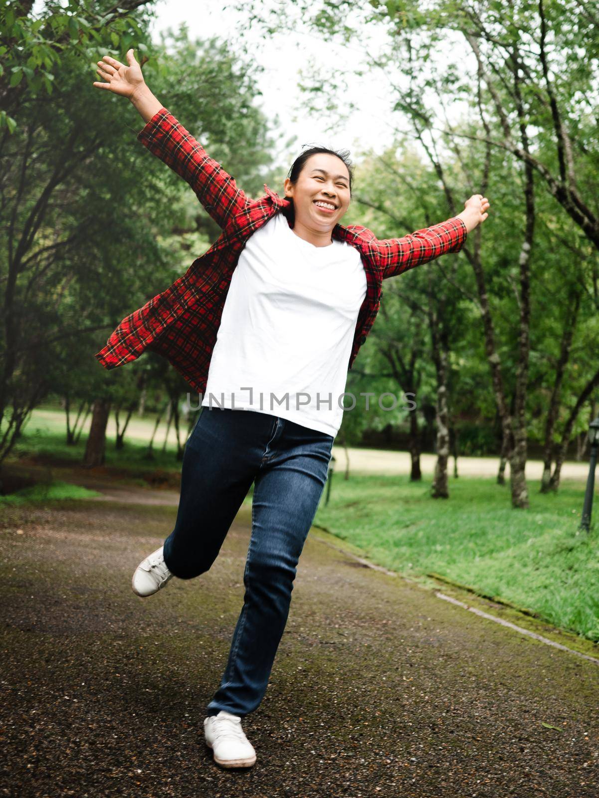 A happy female tourist looking up at the sky with her arms raised enjoying the nature in the forest. Lifestyle on vacation. by TEERASAK