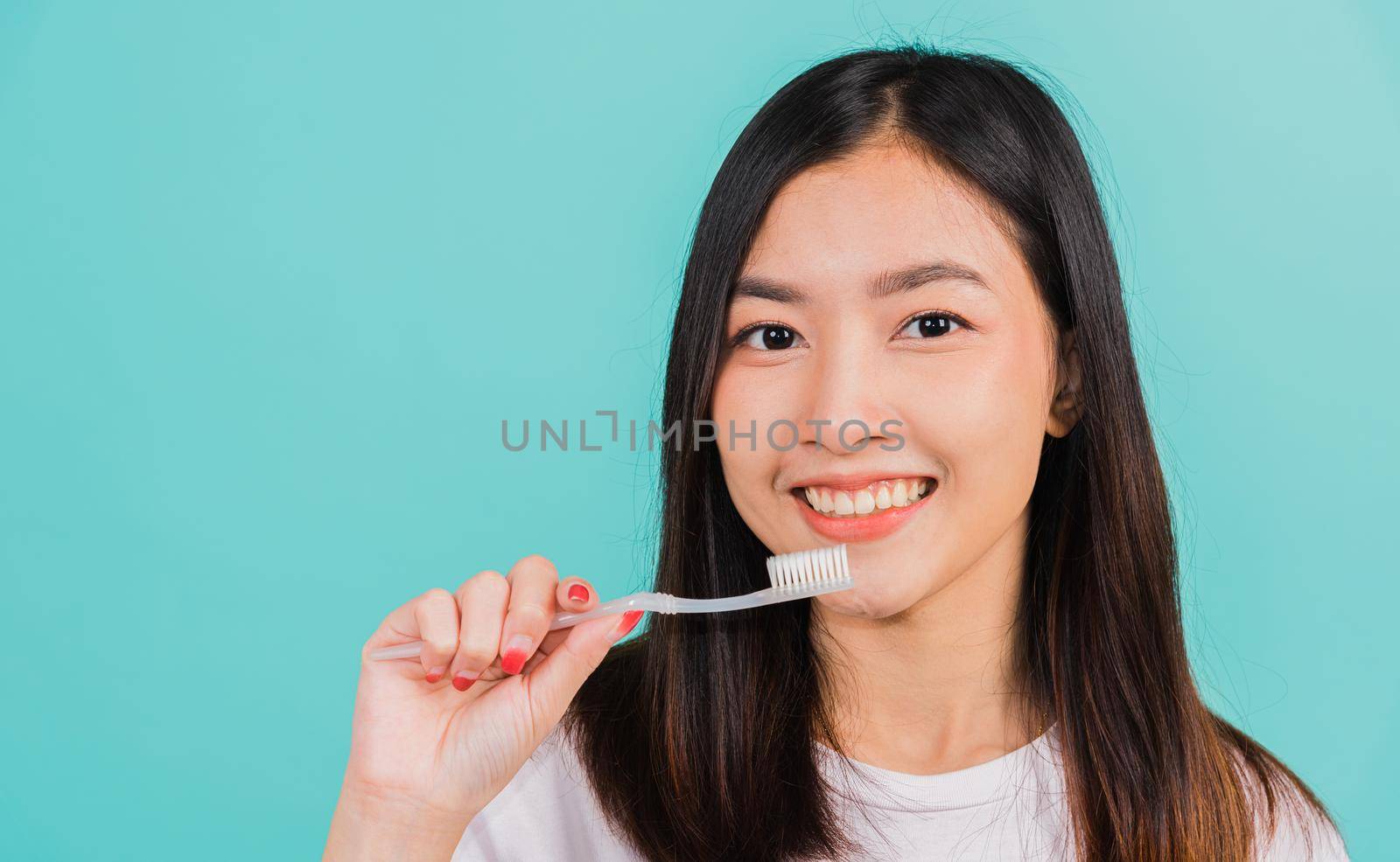 Asian beautiful young woman teen brushing teeth in the morning, portrait of happy Thai female confident smiling holding toothbrush, studio shot isolated on blue background, Dental health concept