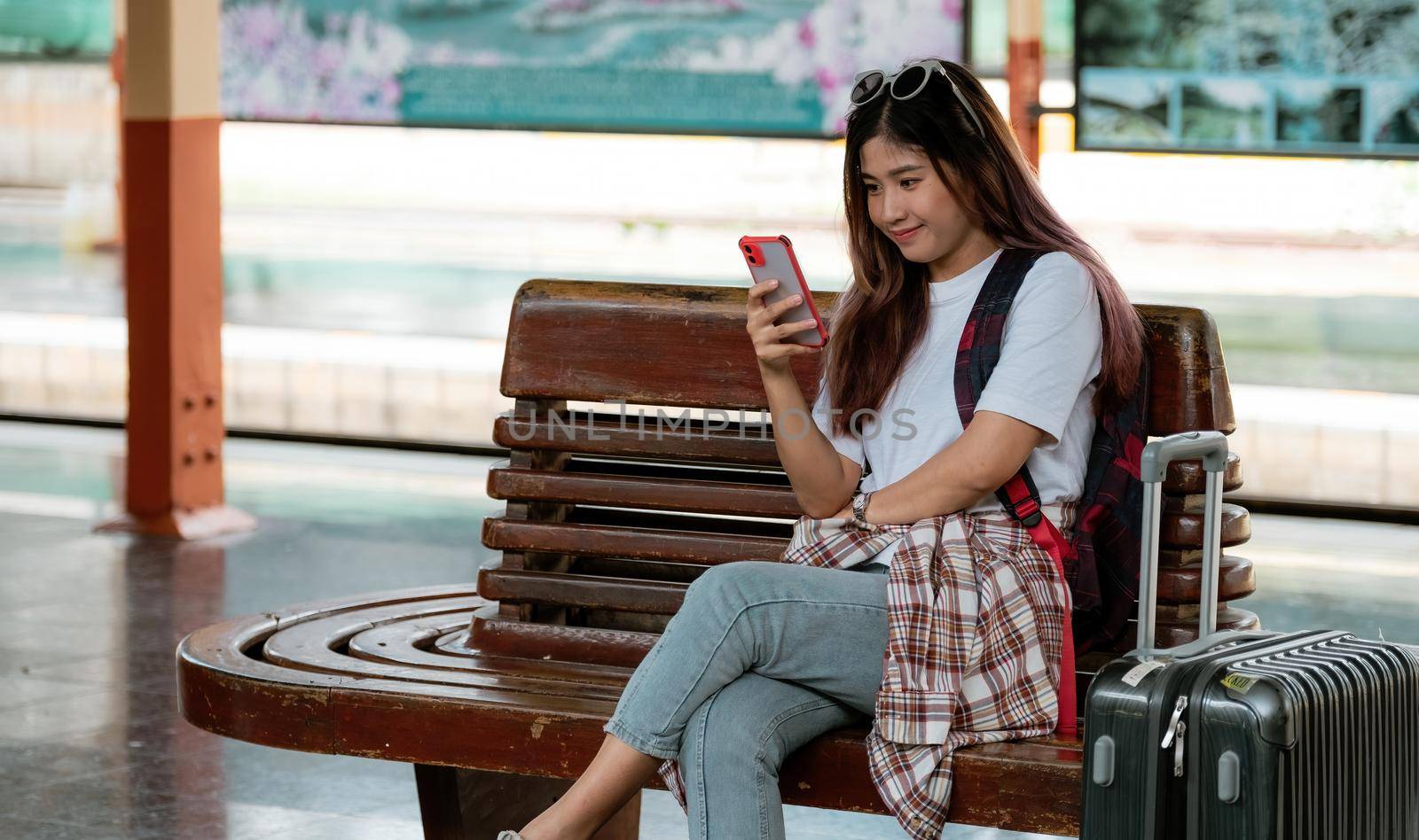 Asian woman wait for train on railway station. travel concept. Traveler using smartphone for online trip planning.