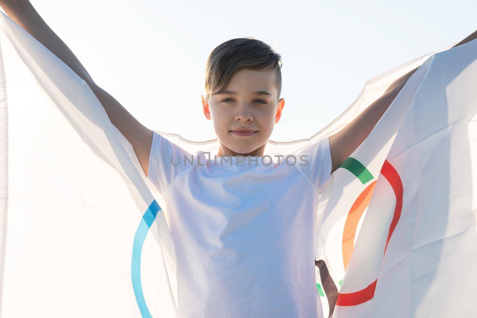 Blonde boy waving waving flag the Olympic Games outdoors over blue sky at the river bank by rusak