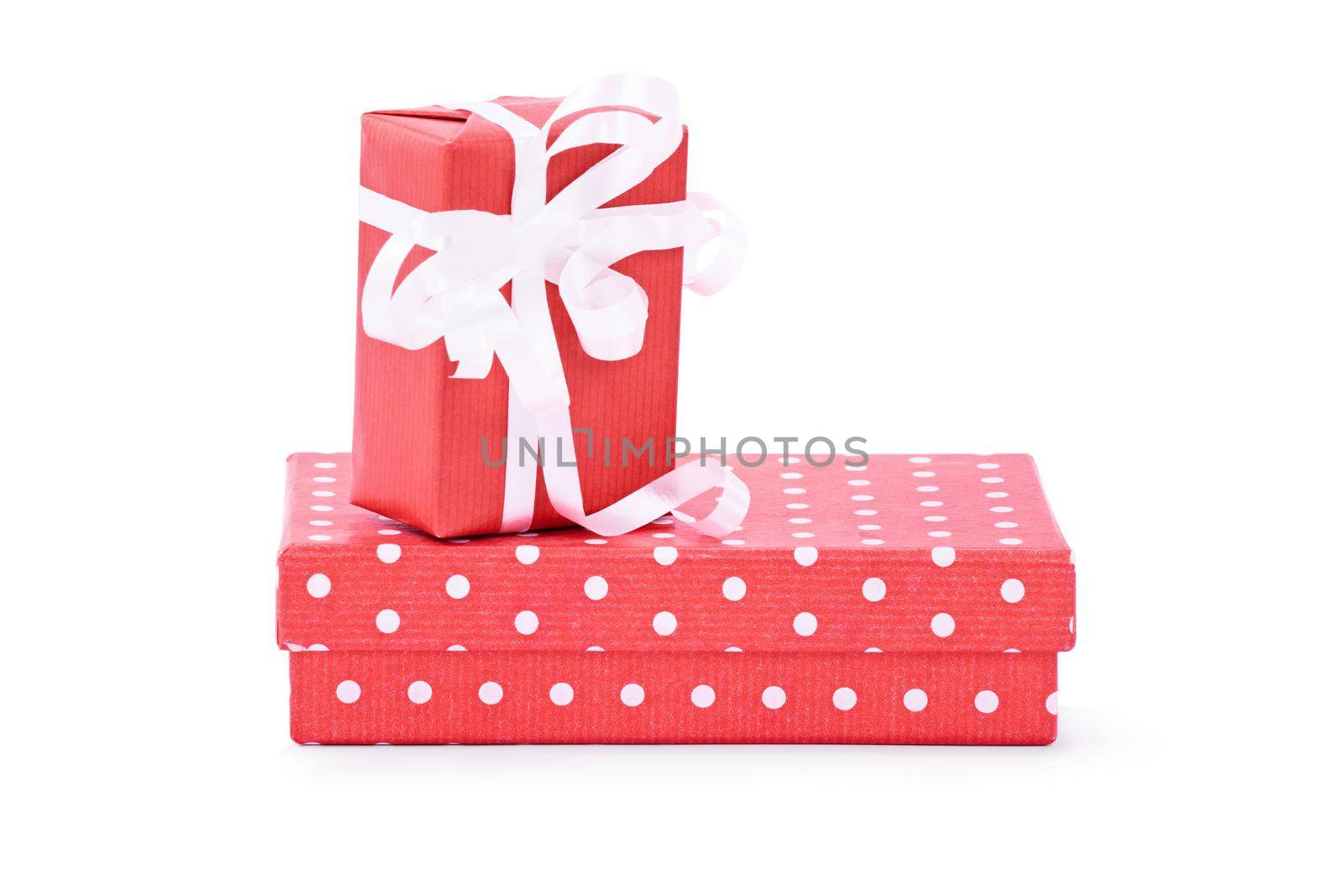 A gift box wrapped in red wrapping paper with white ribbon on top of a red box with polka dots, isolated on white background. Birthday, Christmas, anniversary concept.