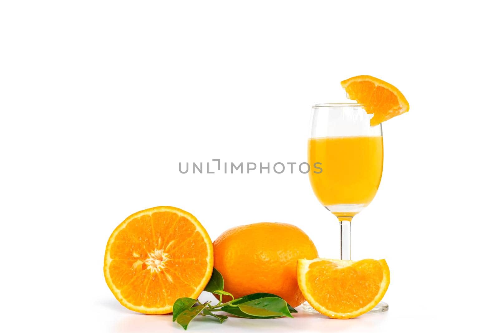 Freshly squeezed orange juice in a glass, decorated with citrus fruits and orange leaves on white background with copy space.