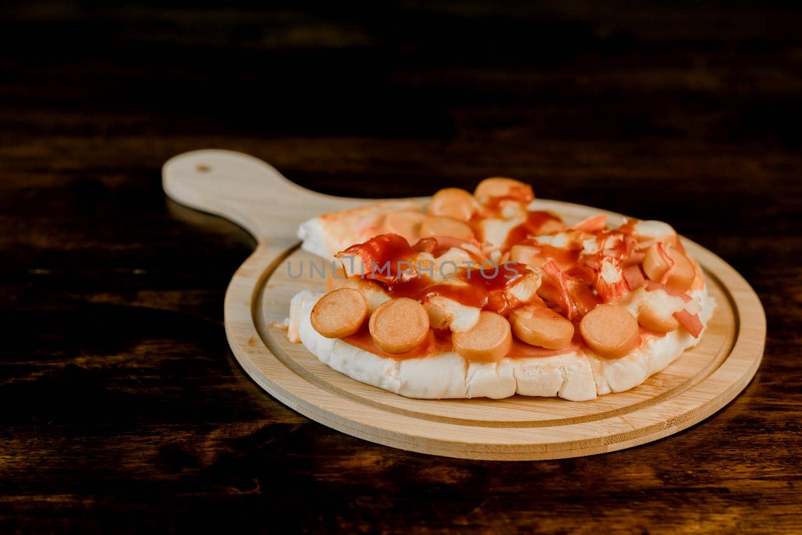 Selective focus of the pizza on a wooden tray on the dark wooden table. by wattanaphob