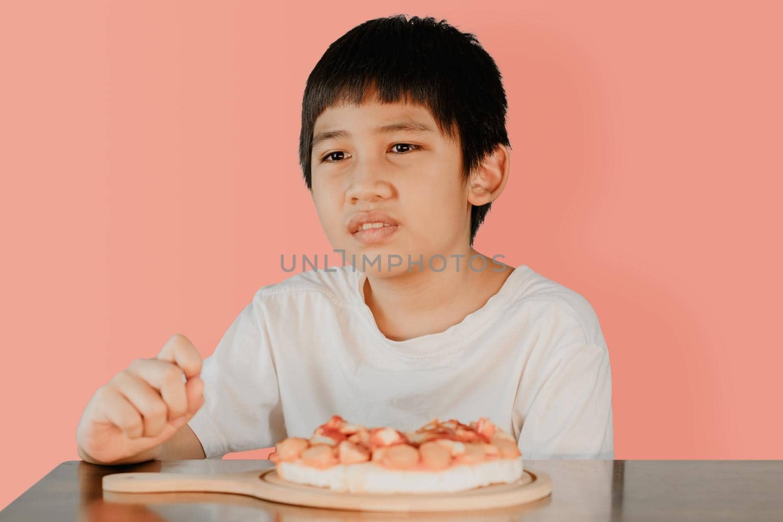 Asian cute boy sitting at the dining table with pizza on the table in front. by wattanaphob