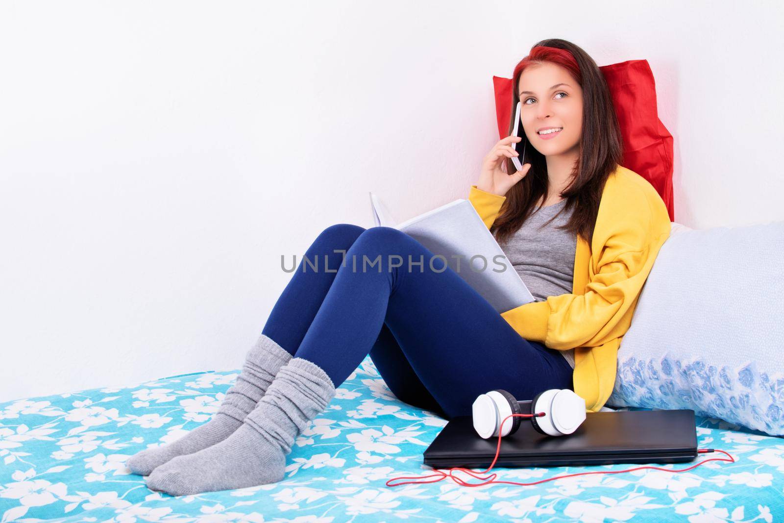 Young girl sitting on her bed talking on a mobile phone by Mendelex