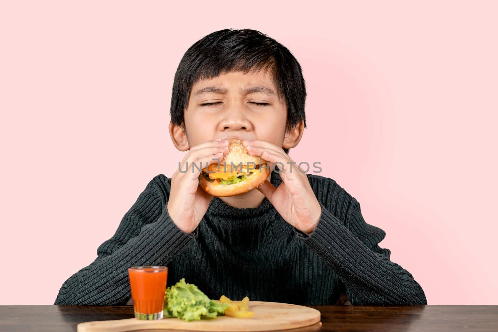 Cute Asian boy eating a delicious hamburger with happiness on pink background.