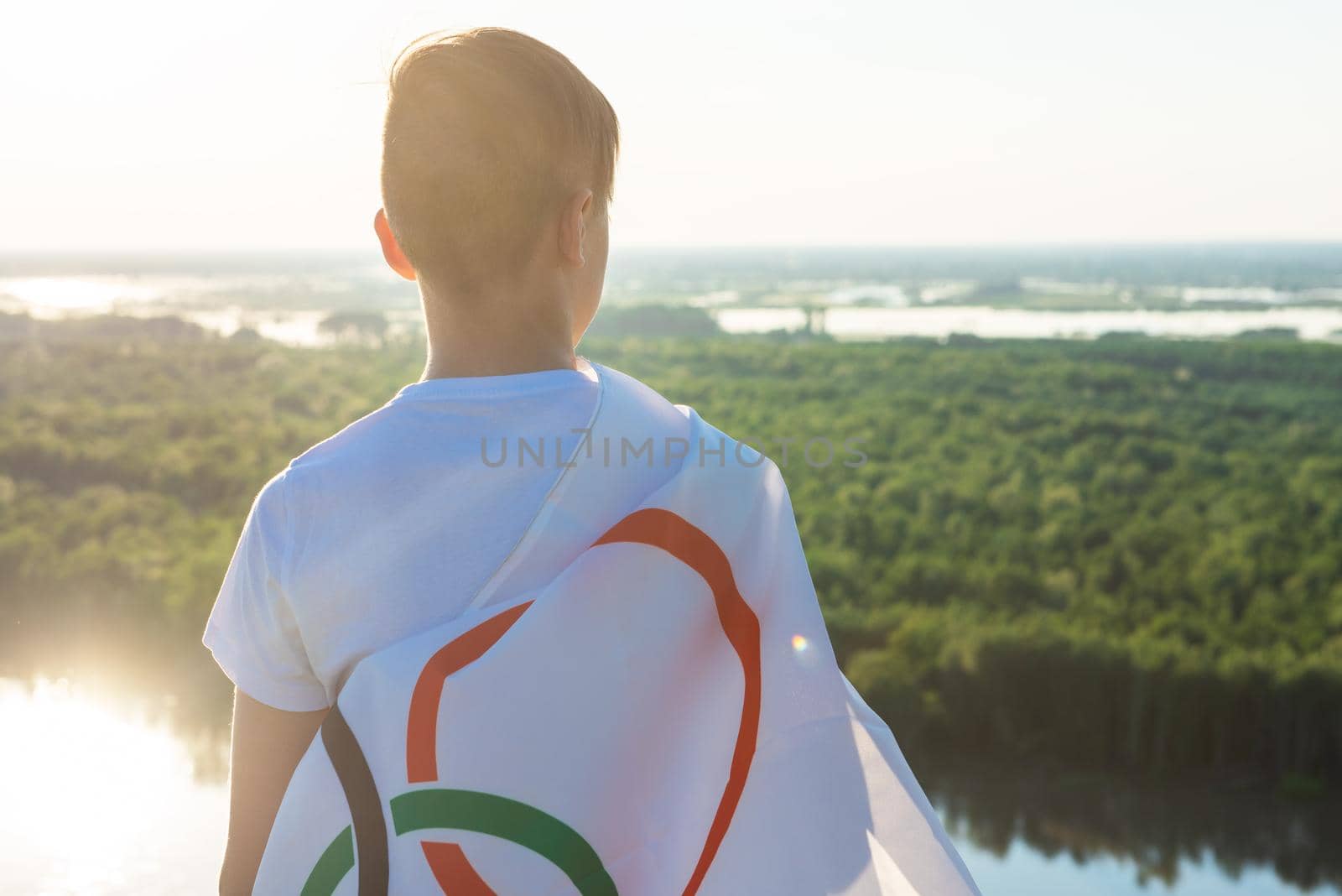 Portrait of boy waving flag the Olympic Games outdoors over cloudy sunset sky. Children sports fan. Summer olympic games concept. 08.06.2021, Barnaul Russia.